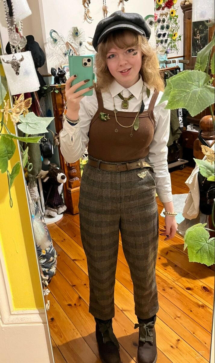Person taking a mirror selfie wearing a brown checkered outfit with a cap indoors.