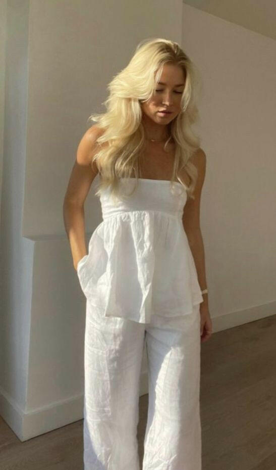 Woman wearing a white outfit standing against a plain wall.