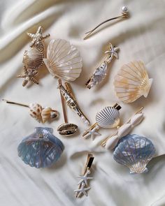 A collection of seashell and starfish-shaped hair pins and barrettes arranged on a draped cream fabric background.