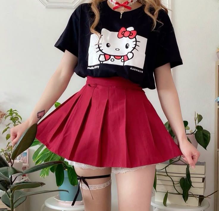 Person wearing a black t-shirt with a cartoon character and a red pleated skirt in an indoor setting.