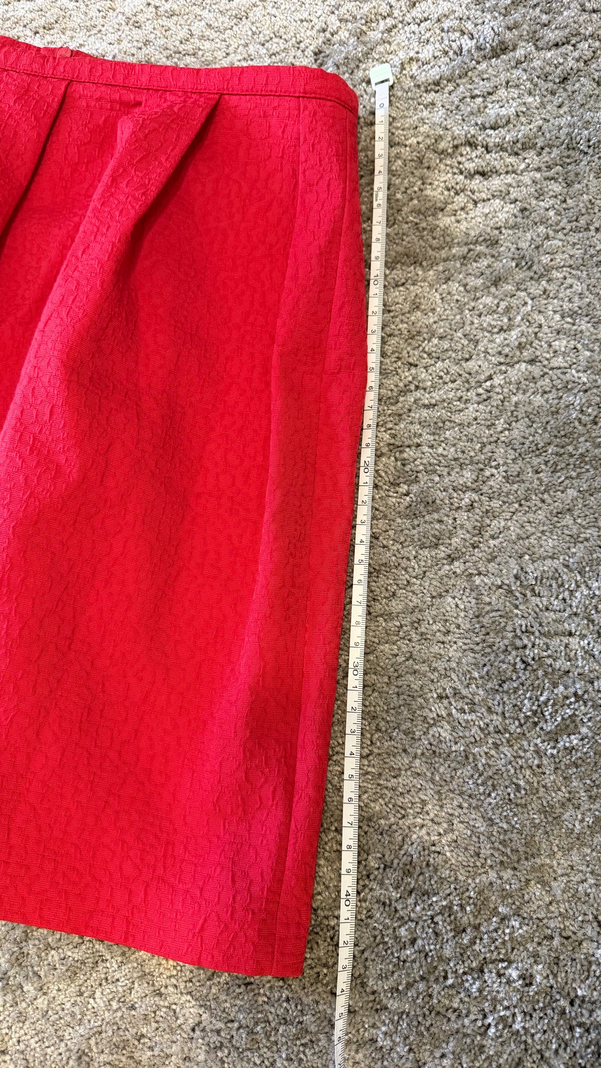 A bright red skirt laid flat on a beige carpet next to a wooden tape measure to show the length.