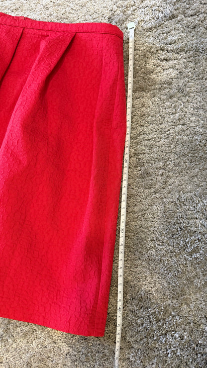 A bright red skirt laid flat on a beige carpet next to a wooden tape measure to show the length.