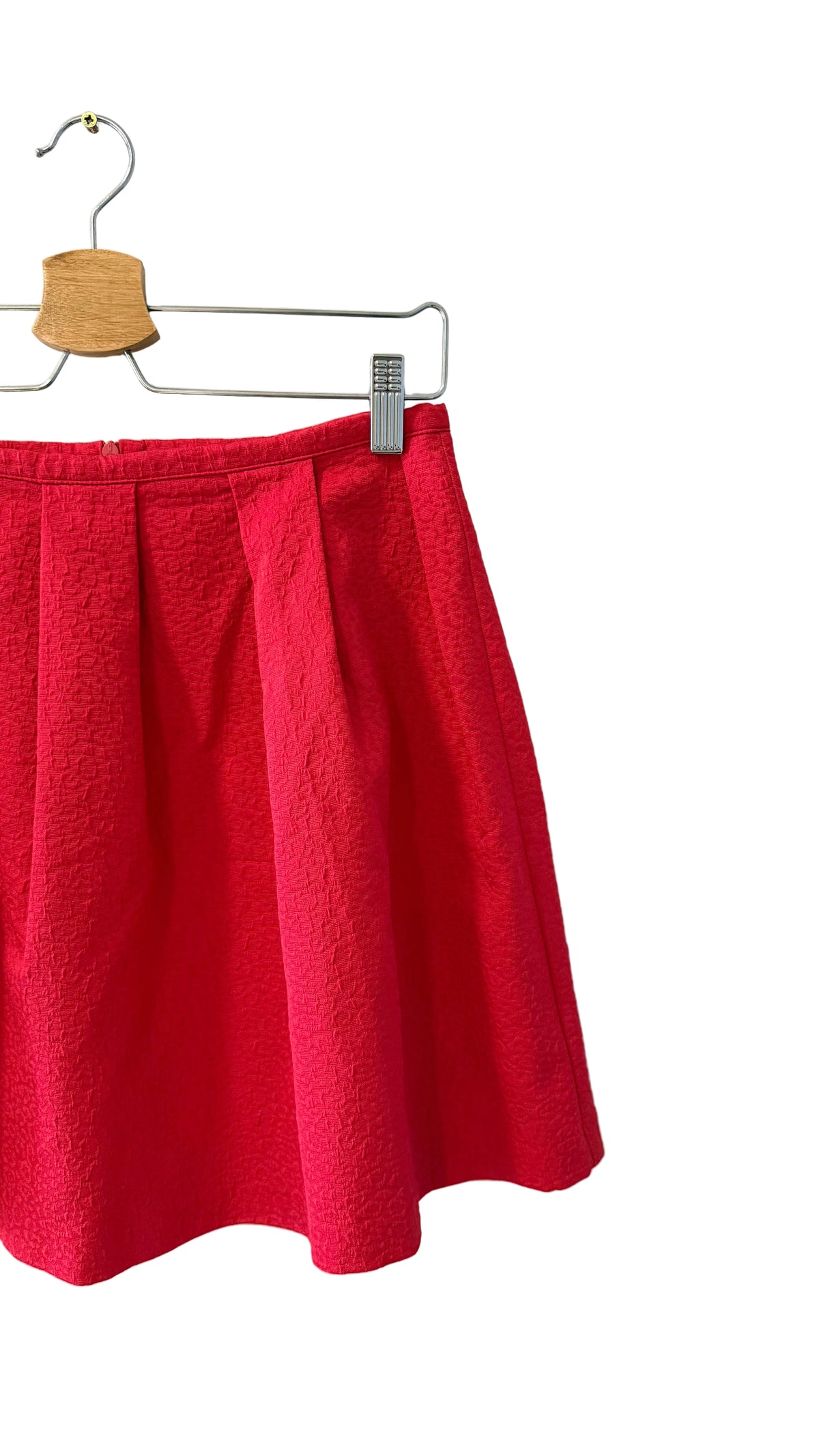 A bright red textured skirt hanging from a metal hanger with a wooden top, shown against a plain white background.