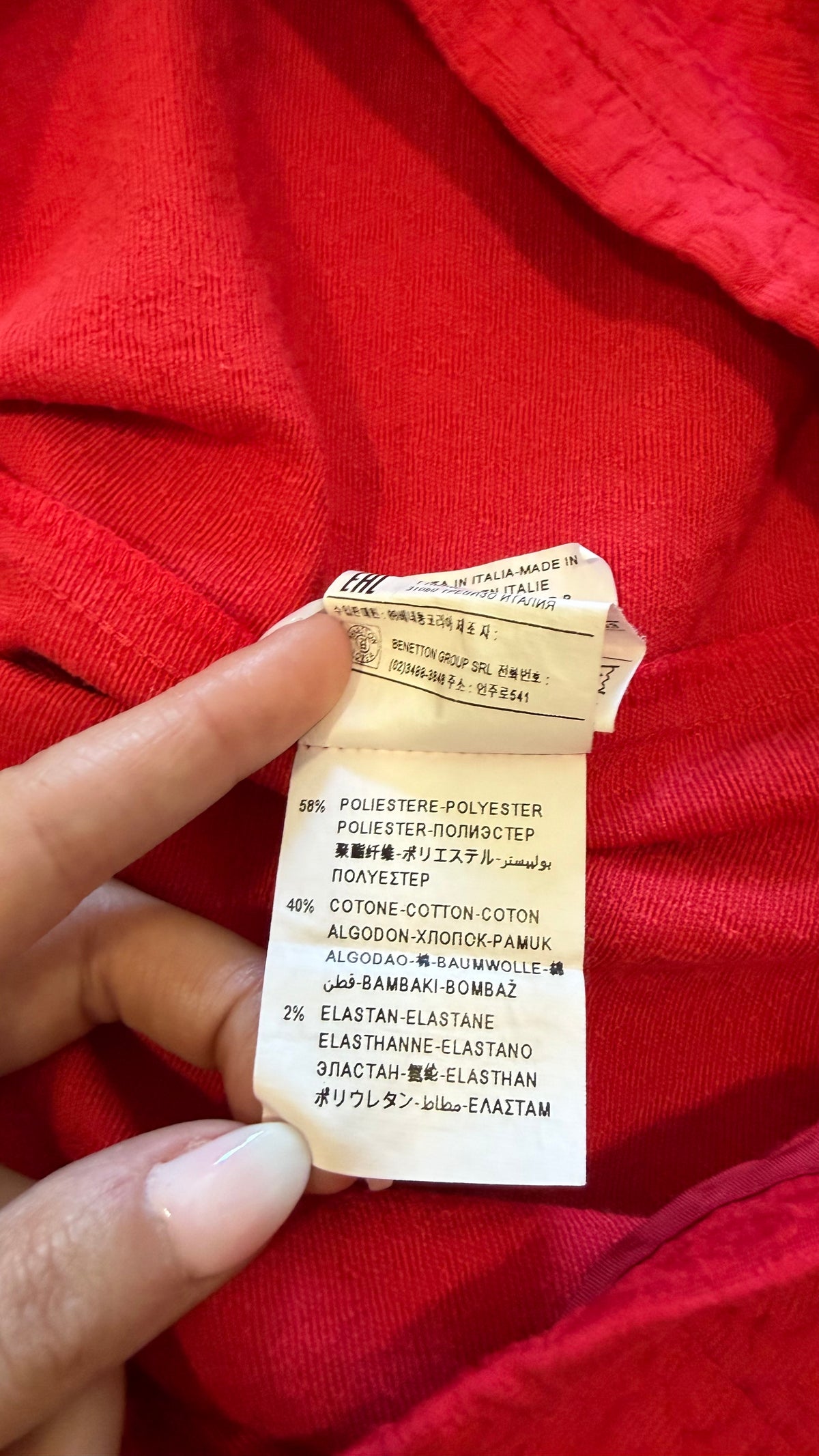 A close-up of a hand holding a fabric care label attached to a bright red knit garment.
