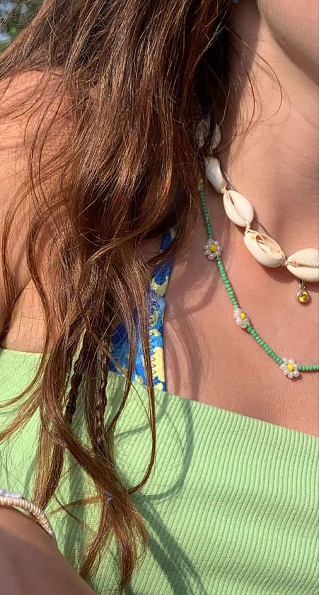 Close-up of a person wearing a green beaded necklace with cowrie shells and small flower charms, paired with a light green ribbed top.