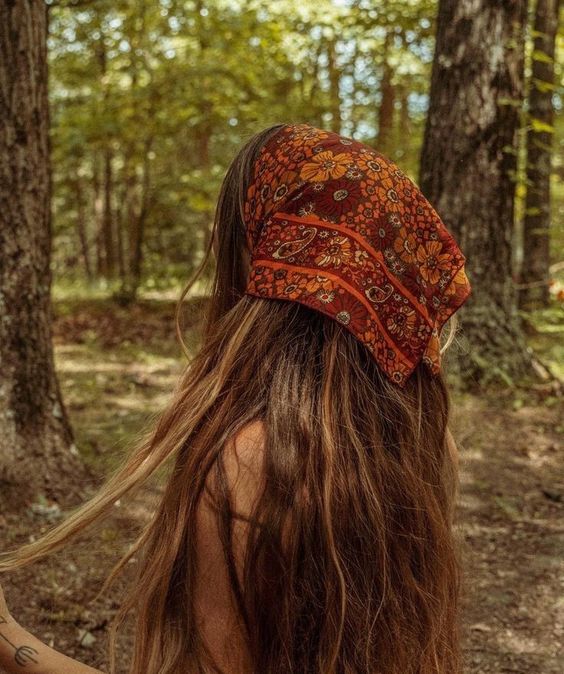 A woman in a forest wearing a rust-orange paisley bandana headscarf, viewed from behind to show the fit and pattern of the scarf.